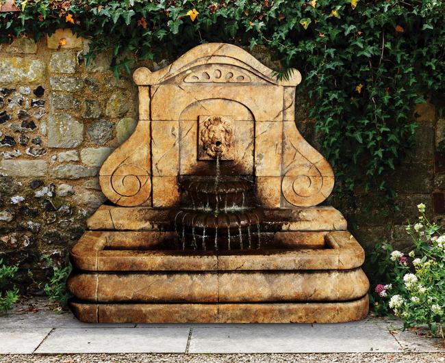 Outdoor fountain with a lion's head spouting water into a basin, mounted on a wall.
