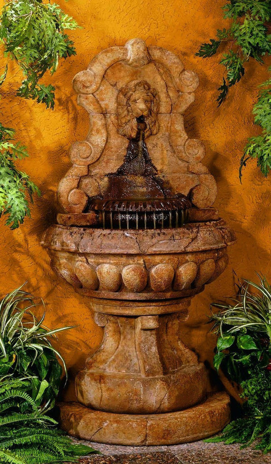 Outdoor fountain with a lion's head spouting water into a basin, set against a wall.
