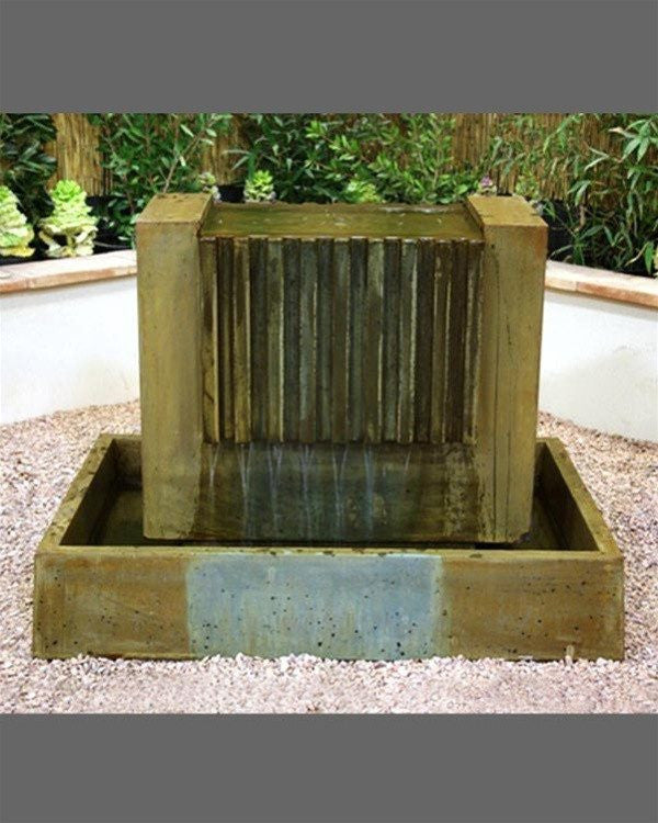 A water fountain with multiple tiers and cascading water, surrounded by lush greenery.