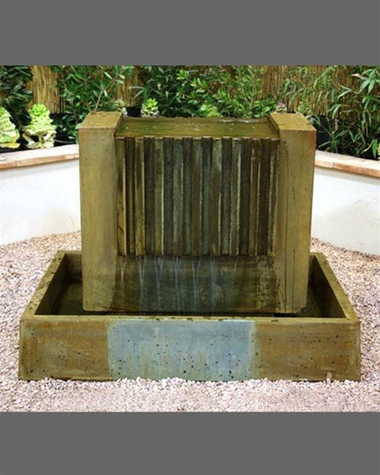 A water fountain with multiple tiers and cascading water, surrounded by lush greenery.