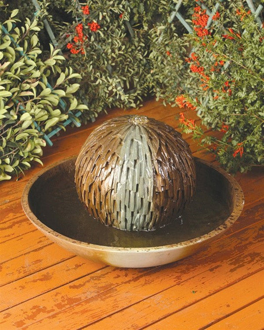 A small, cube-shaped water fountain with a design resembling a Rubik's Cube, set in a garden.